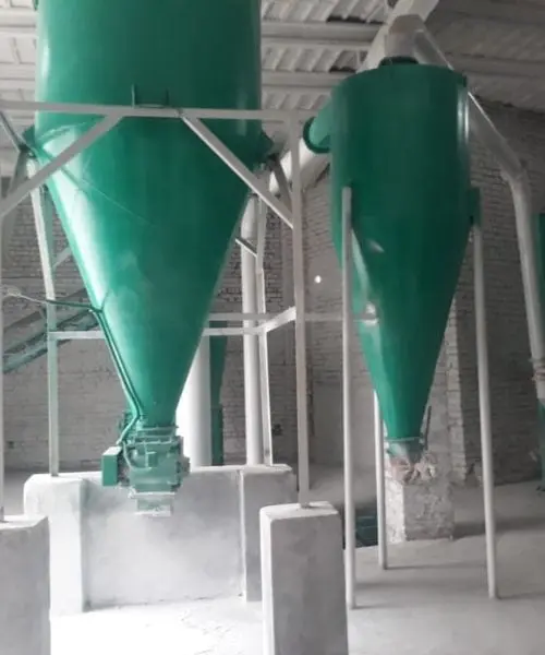 Two green cone hoppers on steel frames inside a processing building