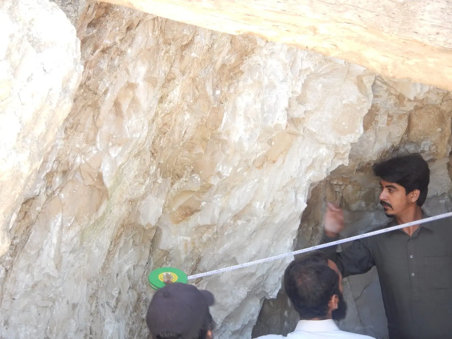 Team members stretching a measuring tape across a pale rock cavity