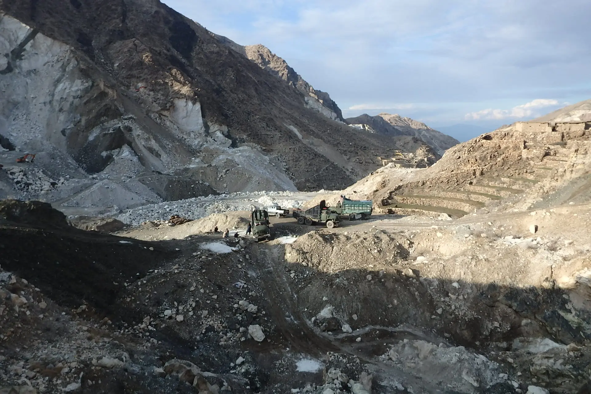 A rocky hillside mine site with terraced cuts and trucks on a haul track
