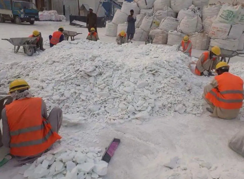 Workers in hard hats sorting white mineral lumps beside filled bulk bags